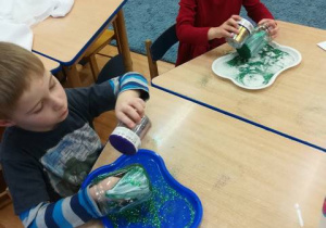 Dzieci posypują pomalowane słoiczki brokatem.